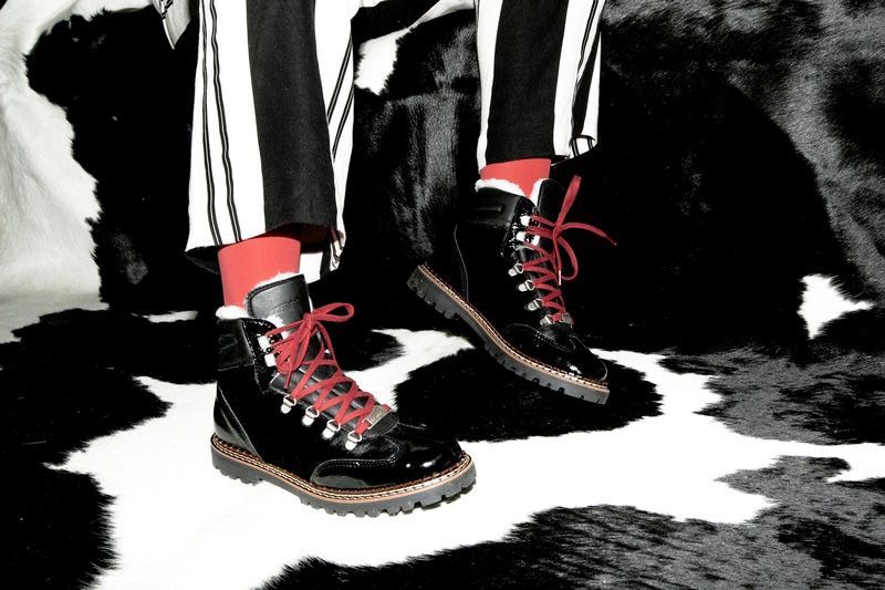 Bottes noires à lacets et chaussettes rouges, pantalon rayé sur un tapis en peau de vache.