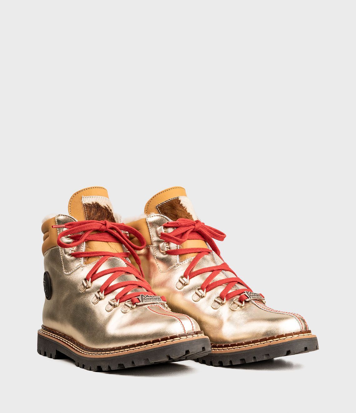 Chaussures de randonnée dorées avec lacets rouges sur fond blanc.