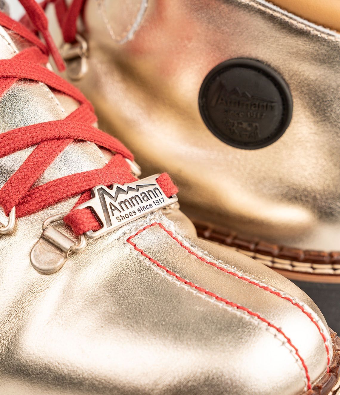 Chaussures de randonnée dorées avec lacets rouges sur fond blanc.