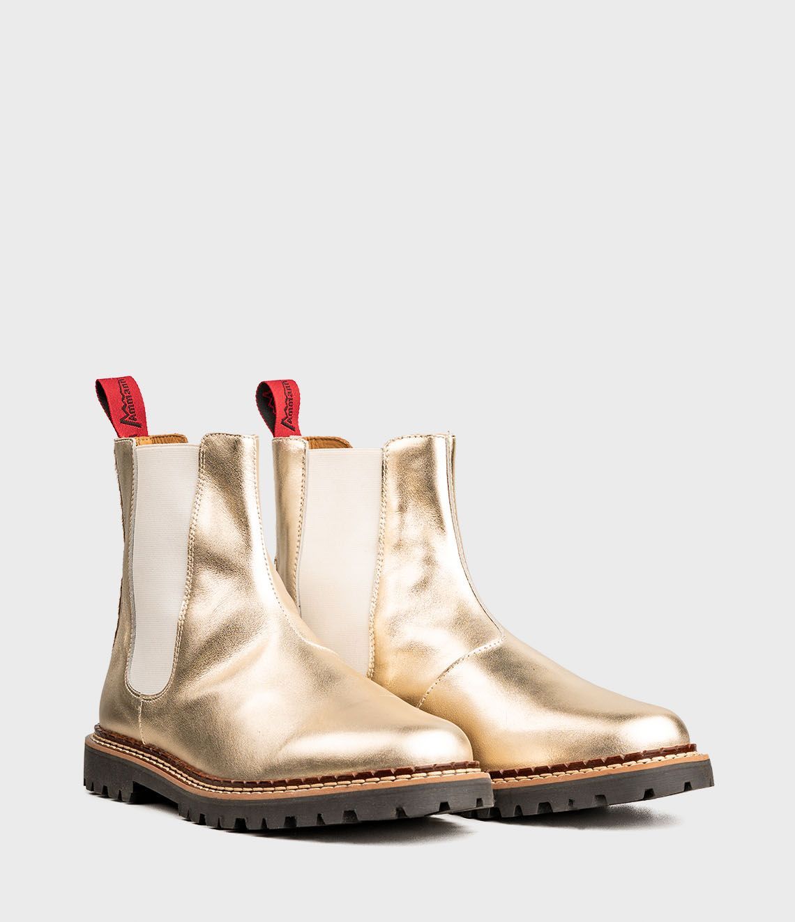 Bottines Chelsea dorées avec tirettes rouges, empiècements latéraux élastiques blancs et semelles foncées.