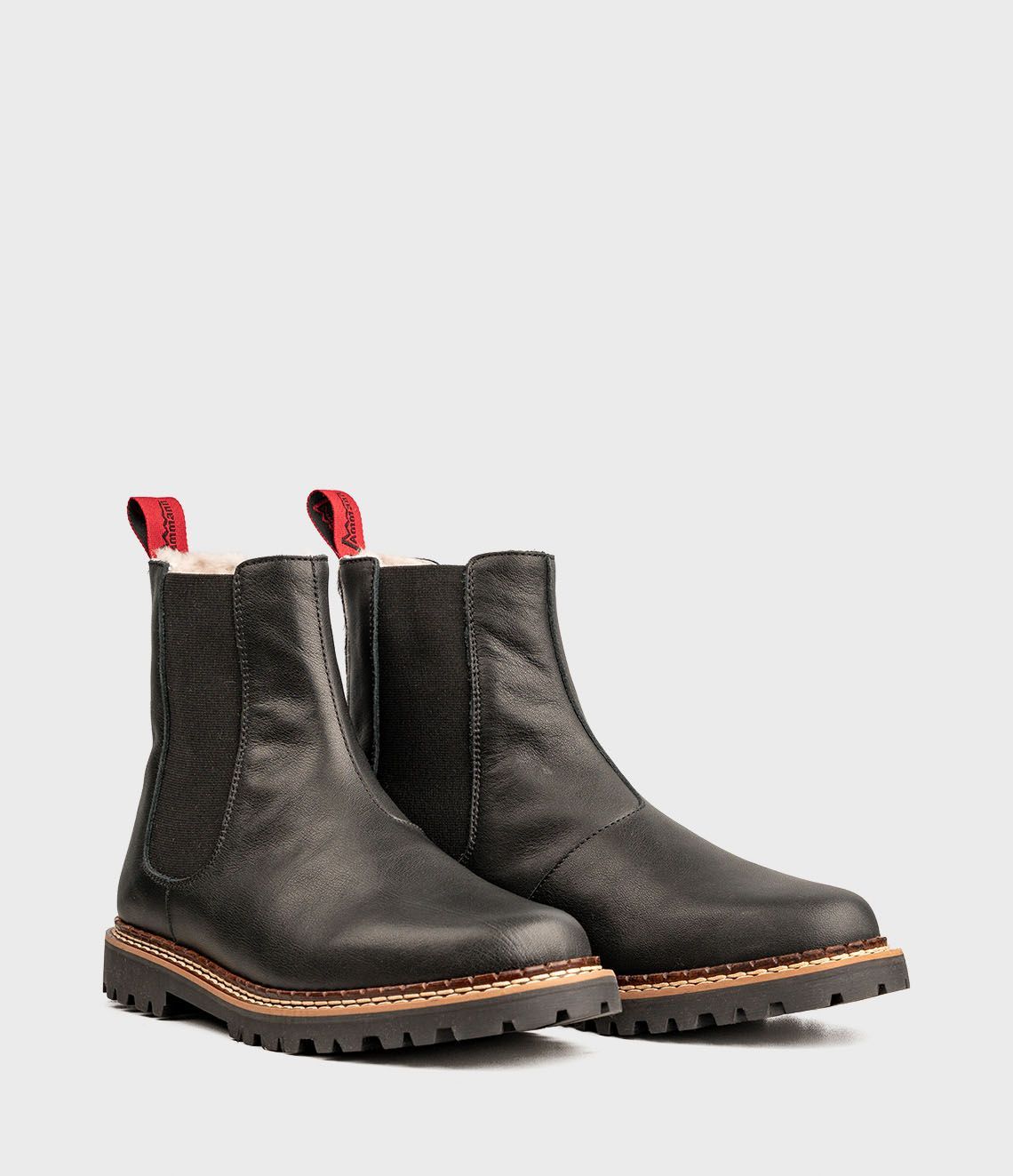 Bottines Chelsea en cuir noir avec tirettes rouges et doublure en peau lainée.