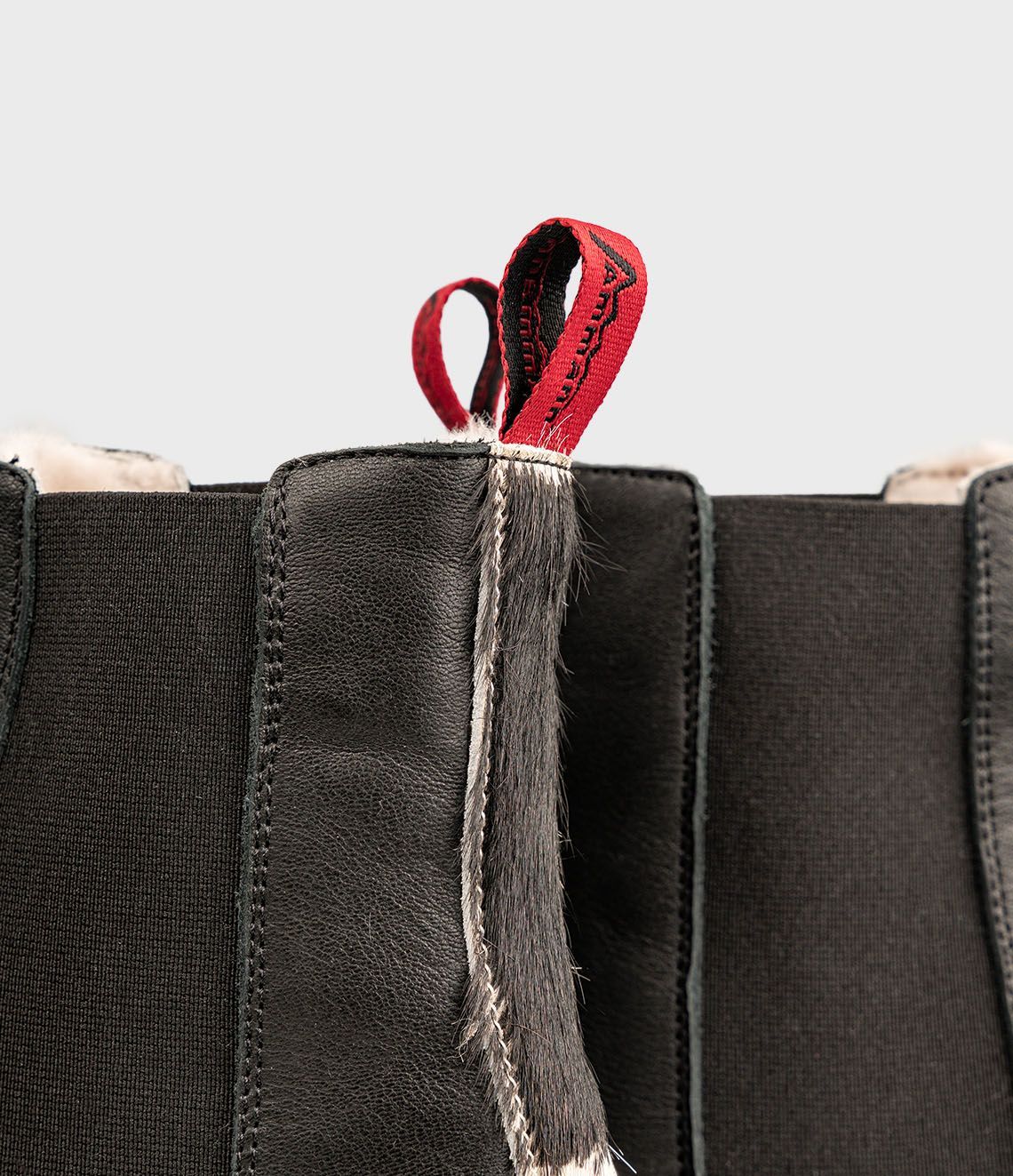 Bottines Chelsea en cuir noir avec tirettes rouges et doublure en peau lainée.