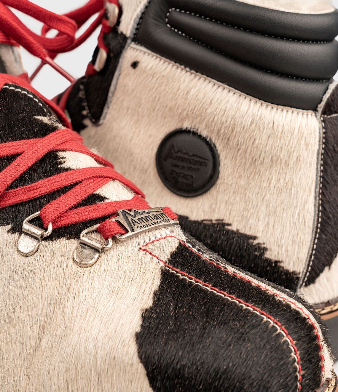 Chaussures de randonnée en cuir de vachette noir et blanc avec lacets rouges sur fond blanc.