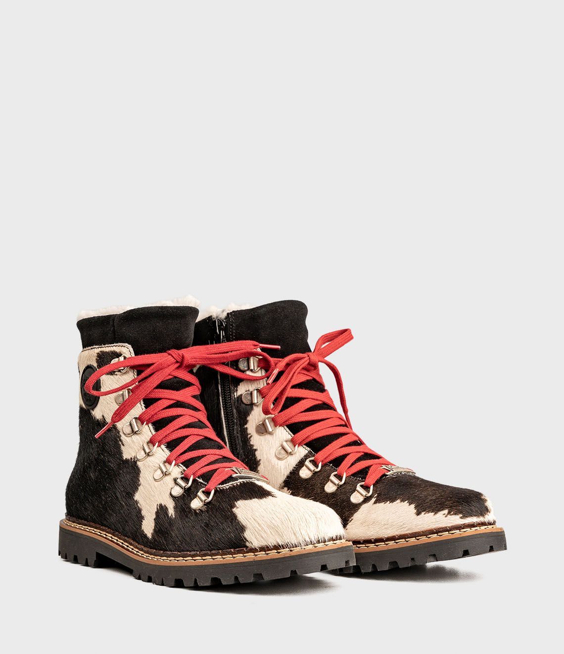 Bottes à imprimé vache noir et blanc avec lacets rouges et semelles noires.