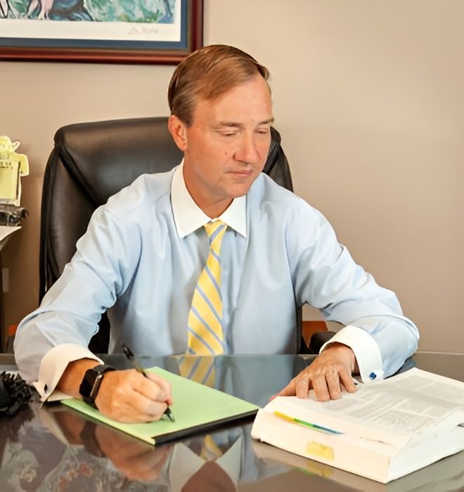 Man in a light blue shirt and striped tie writing at a desk with papers and a binder.
