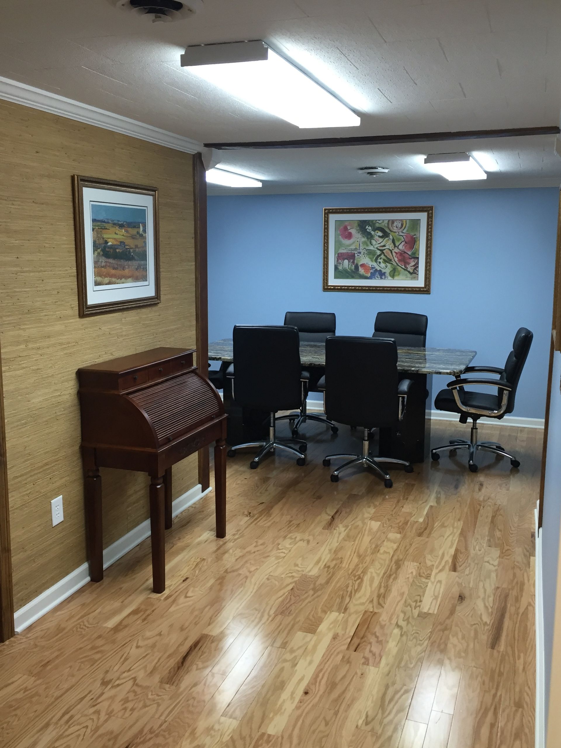 Empty office with blue accent wall, framed art, desks, computers, and a wooden roll-top desk on hardwood floors
