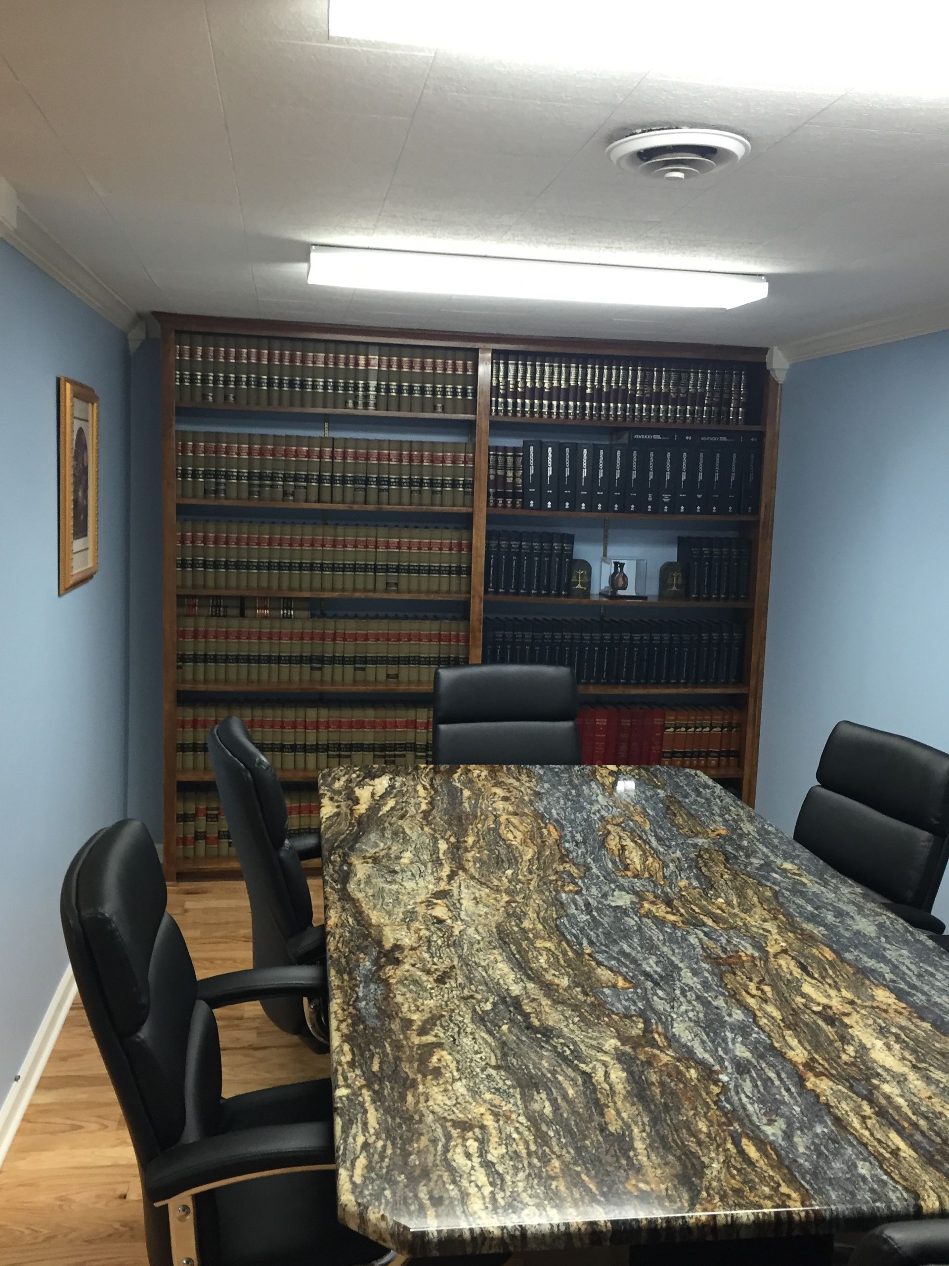 Conference room with a long marbled table, black chairs, and a wall of bookshelves.