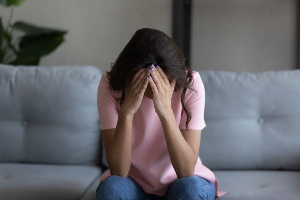 Person sitting on a couch with head in hands, appearing distressed.