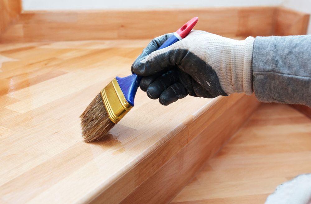 A Person Is Painting a Wooden Staircase with A Brush — Budget Timbers in Coffs Harbour, NSW