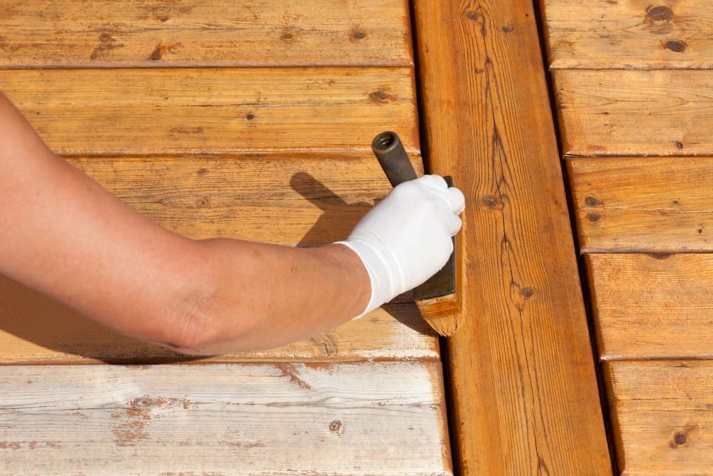 A Person Is Painting a Wooden Deck with A Brush — Budget Timbers in Tweed Heads, NSW