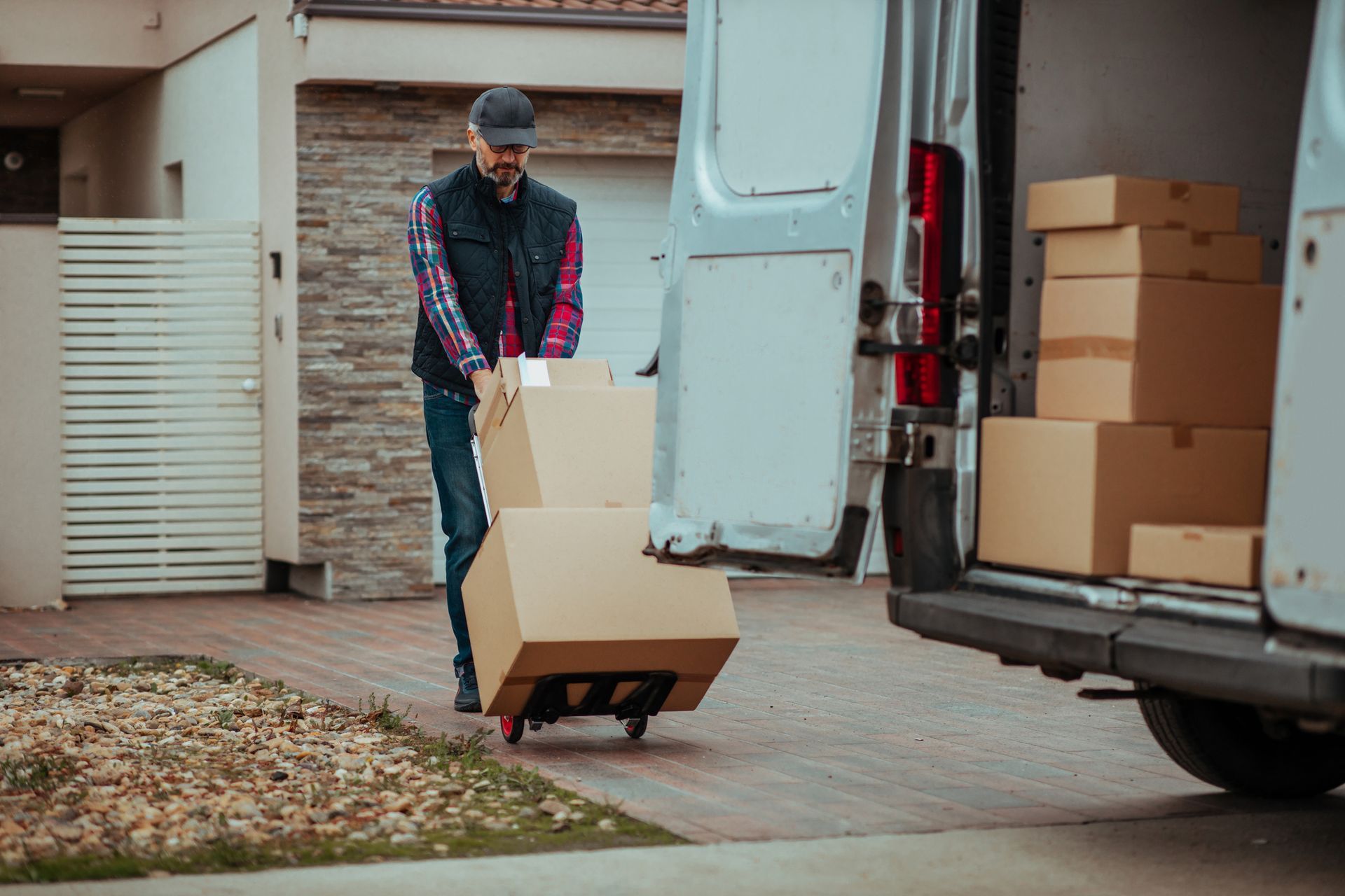 A delivery man is pushing a cart with boxes in front of a van.
