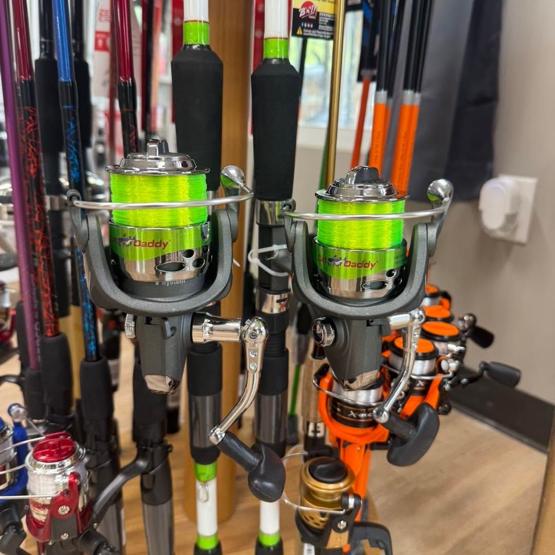 Two neon green fishing reels mounted on rods in a gear rack, with several rods in the background.