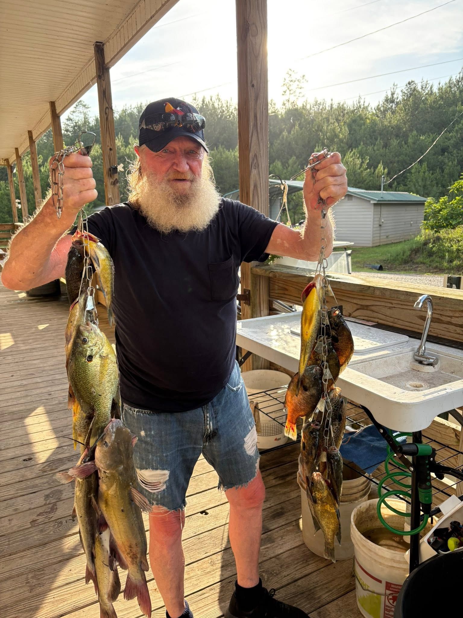 Man holding two large fish by a covered porch, with a table and outdoor yard in the background