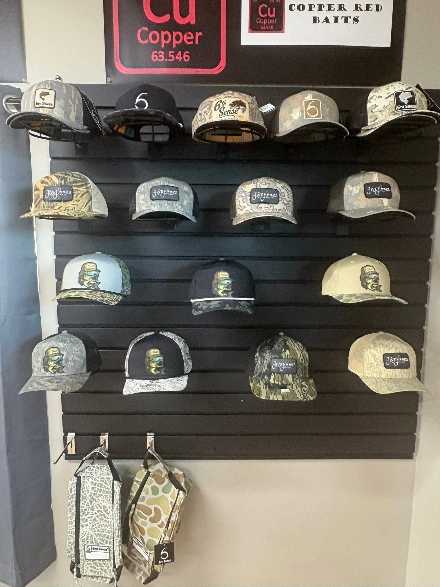 Wall display of assorted baseball caps on black shelves in a shop, with a copper sign above.