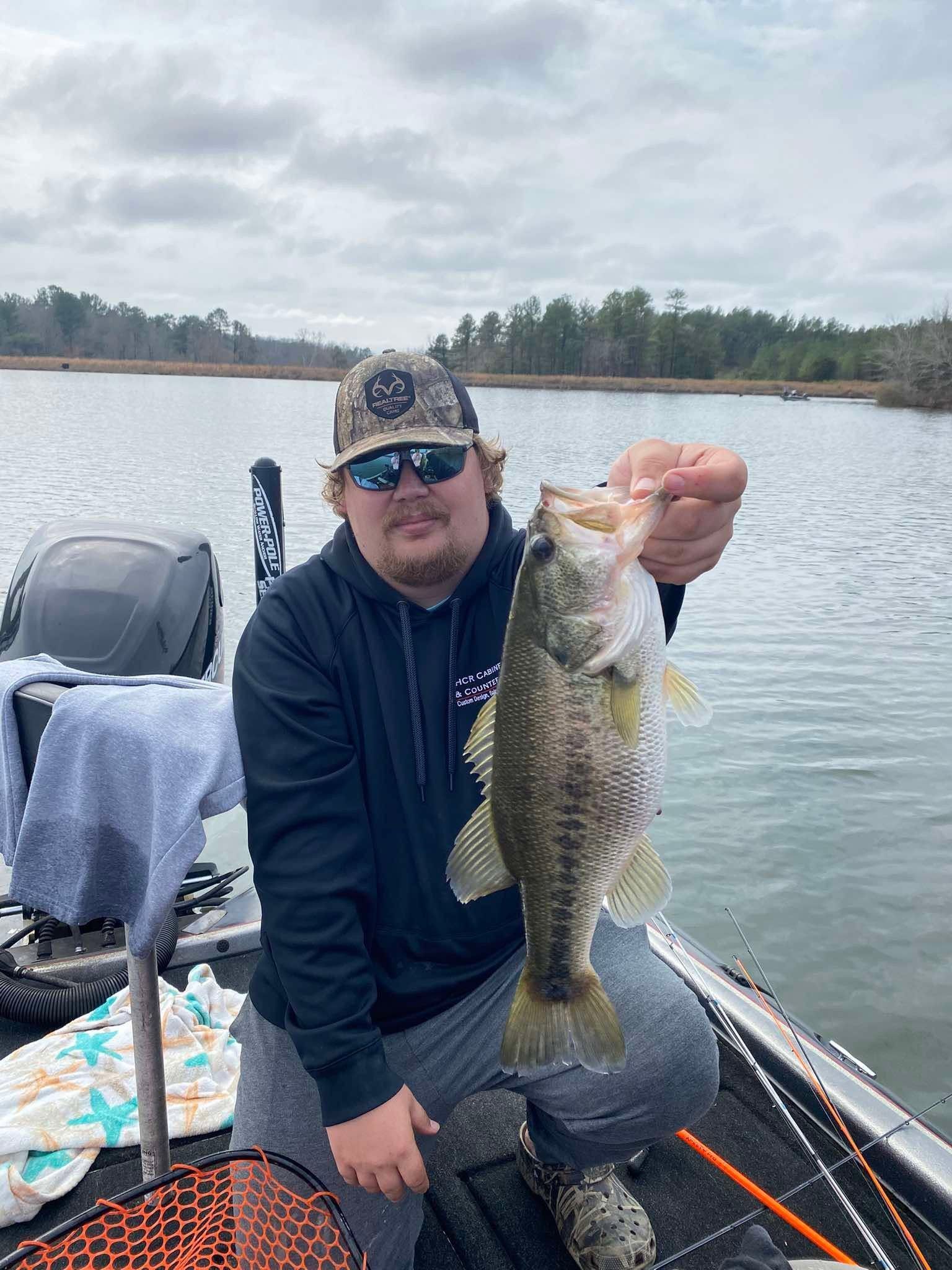Man on a fishing boat holding up a large striped bass on a cloudy lake.