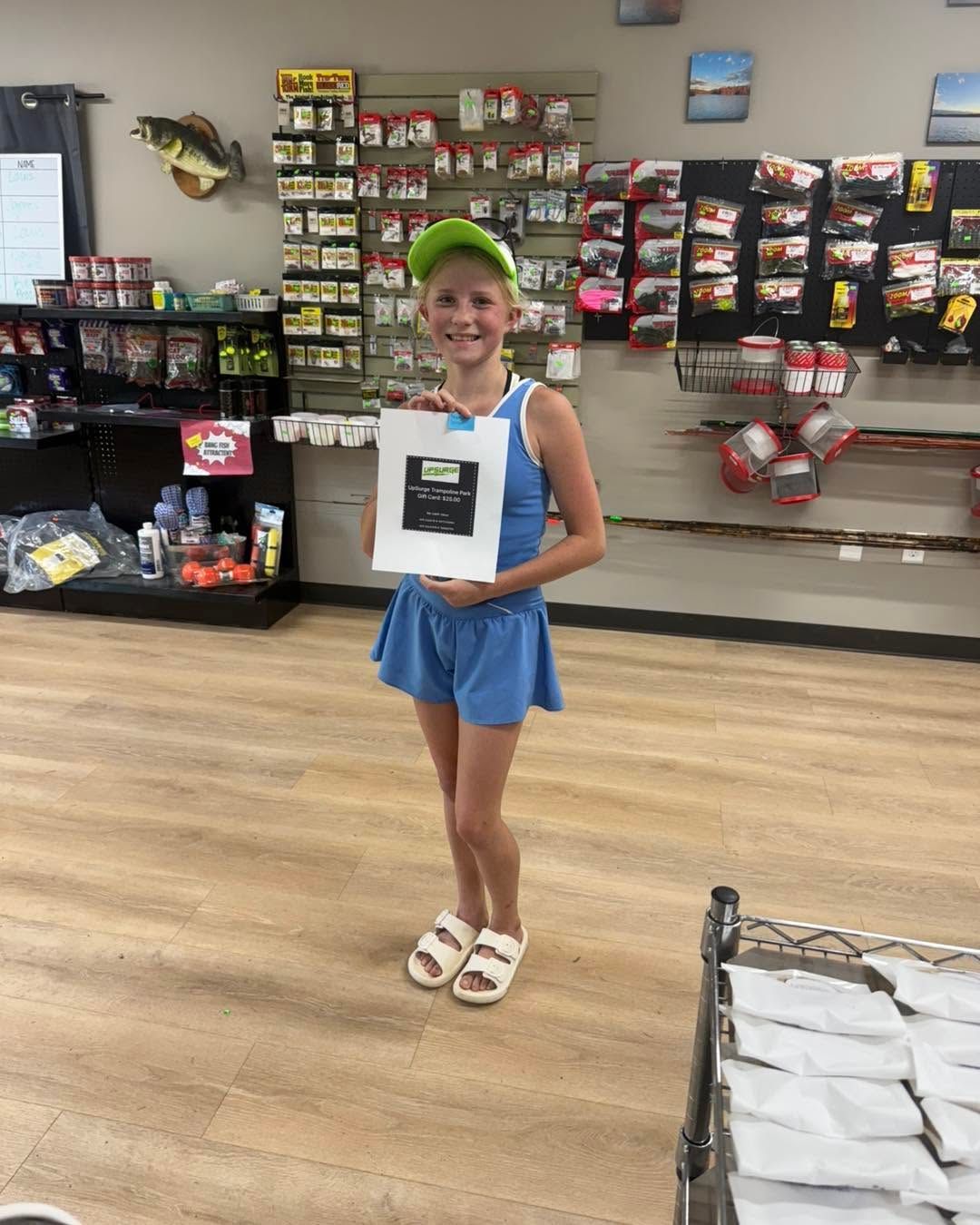 Smiling child in a store, holding a prize bag and standing in front of display shelves.