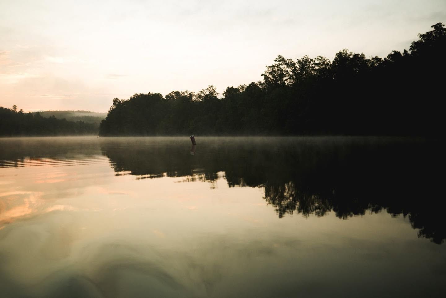 Calm river at sunrise with dark tree silhouettes reflected on the water and a lone figure near the center