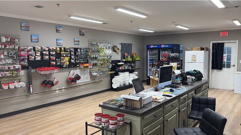 Retail store interior with display shelves, a central counter, and black chairs under bright fluorescent lights