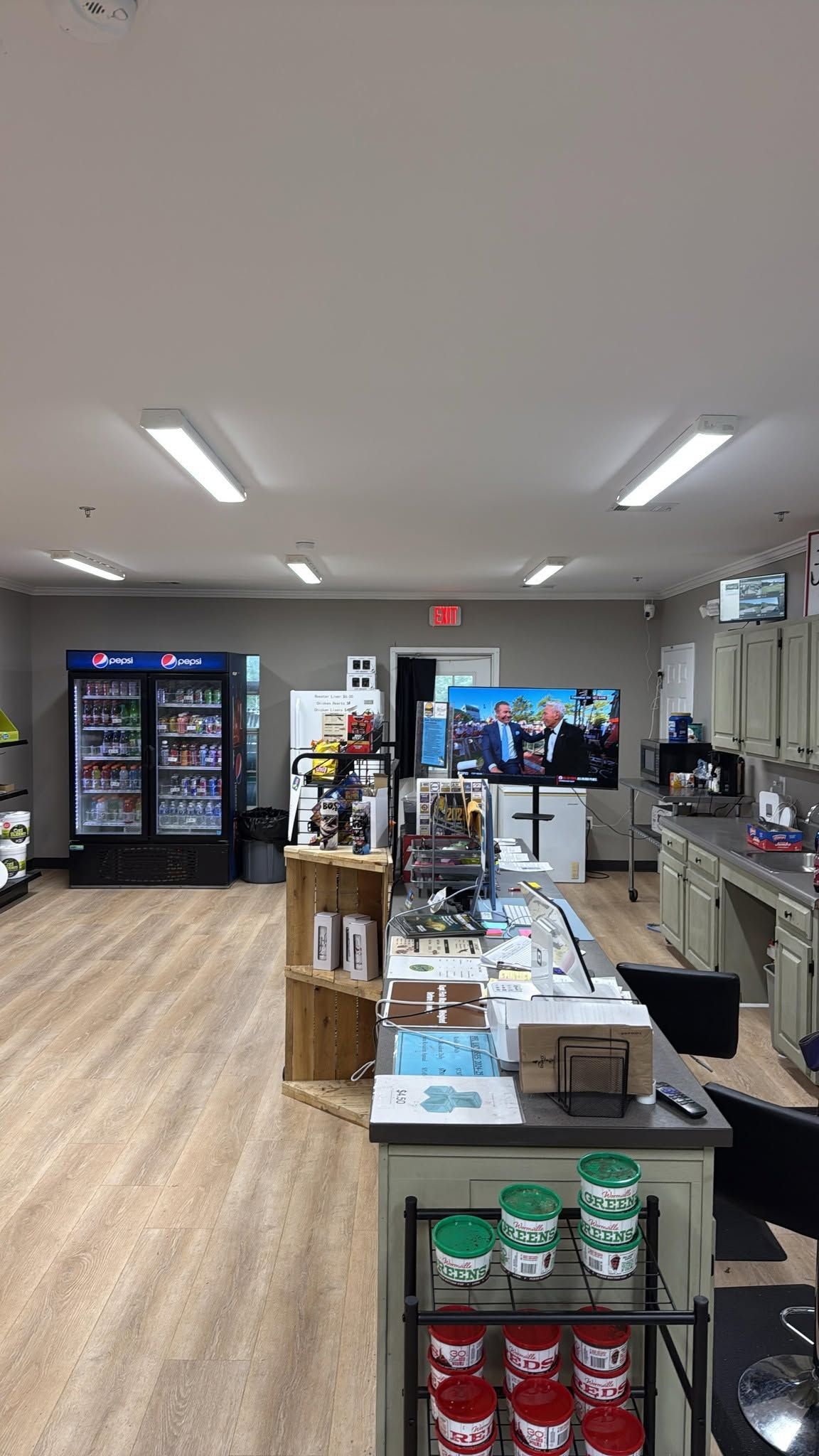 Convenience store aisle with refrigerated drinks, snacks, and checkout counter under bright ceiling lights