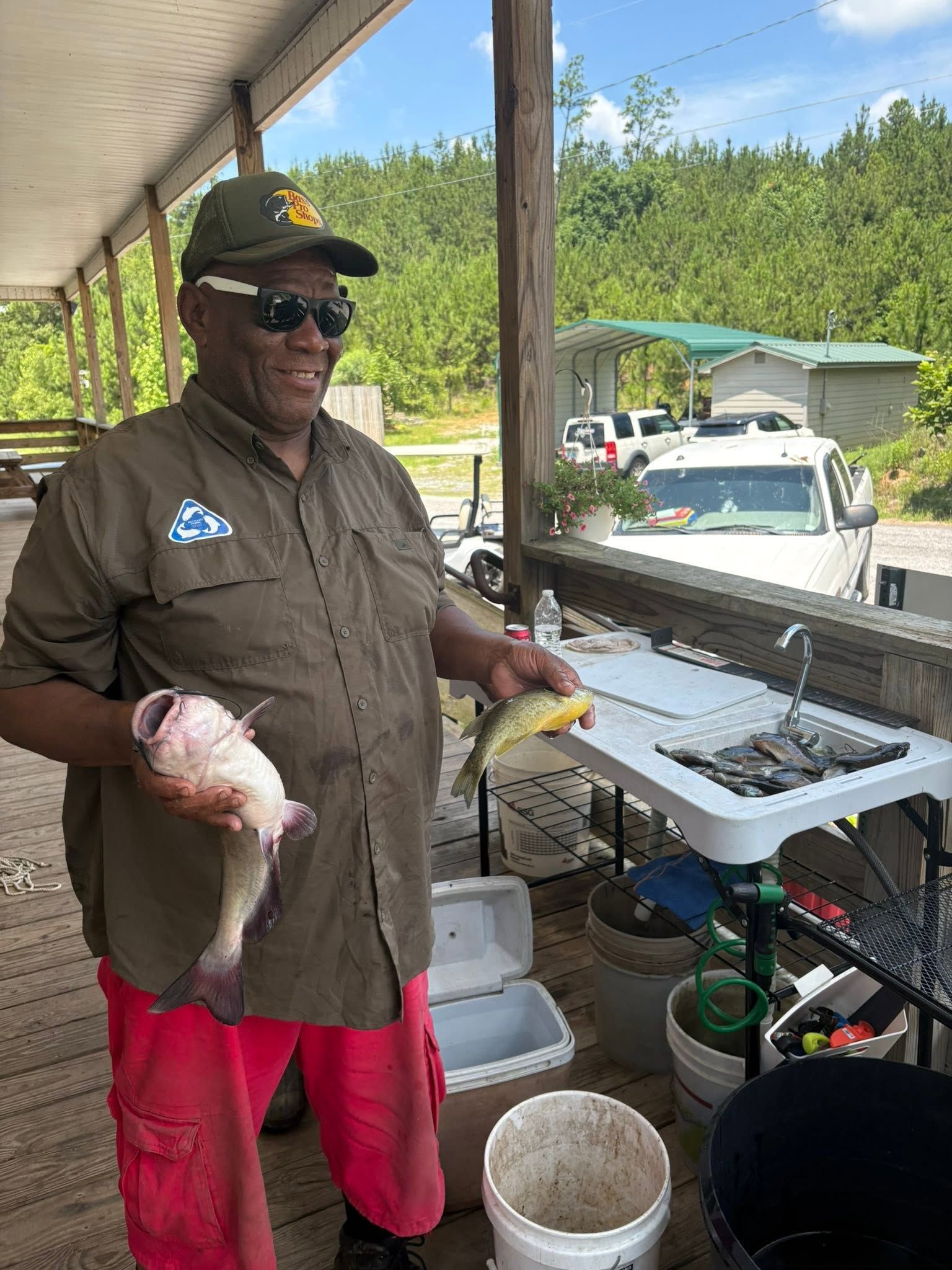 Person holding two fish beside an outdoor cleaning station under a covered shelter.