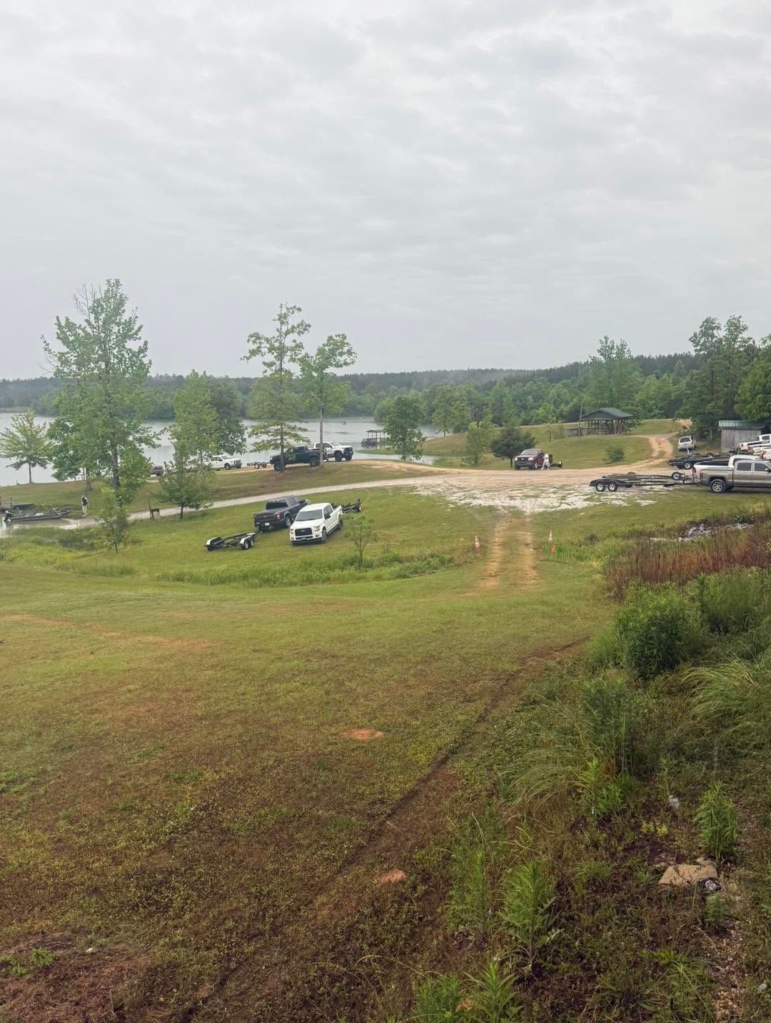 Grassy lakeside field with parked trucks and a dirt track under an overcast sky