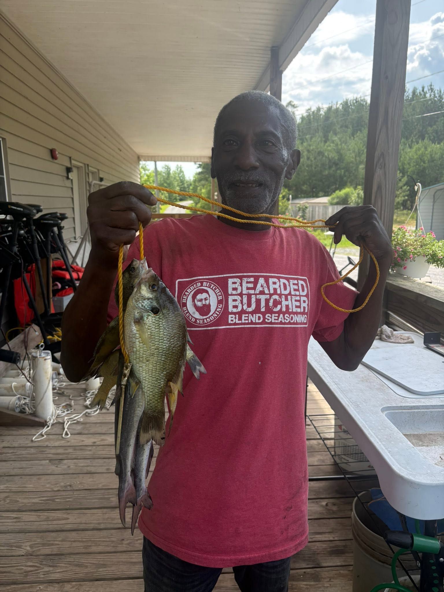 Man holding several fish by a dock, wearing a red T-shirt and smiling.