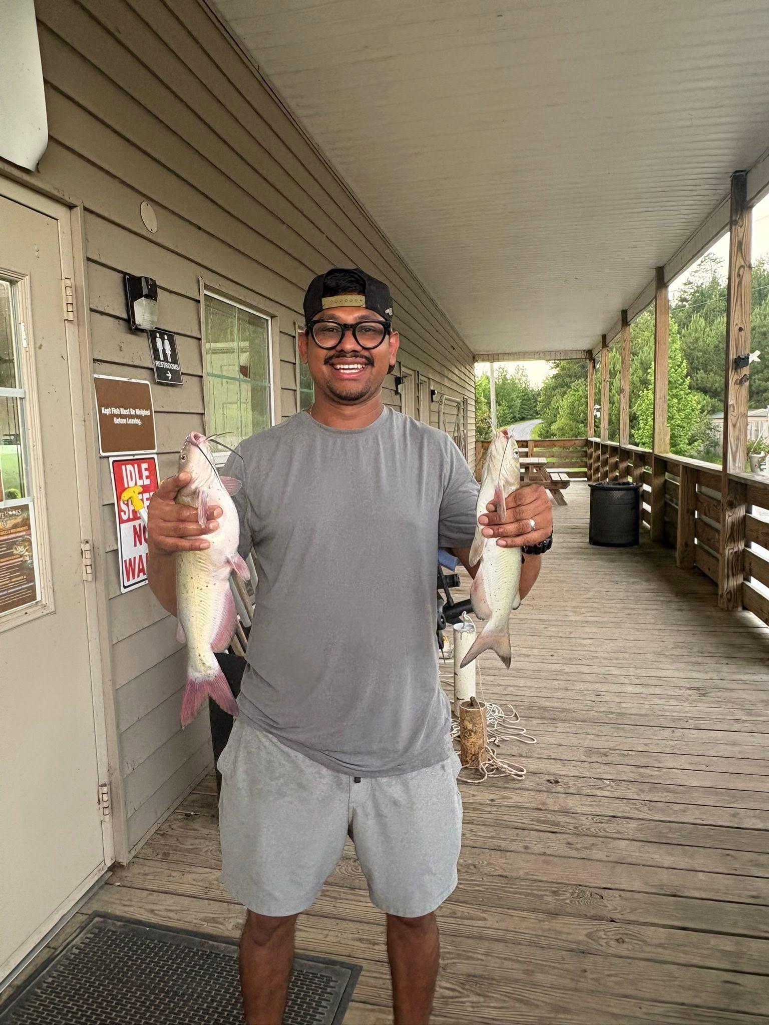 Smiling person on a porch holding two large fish by the tails