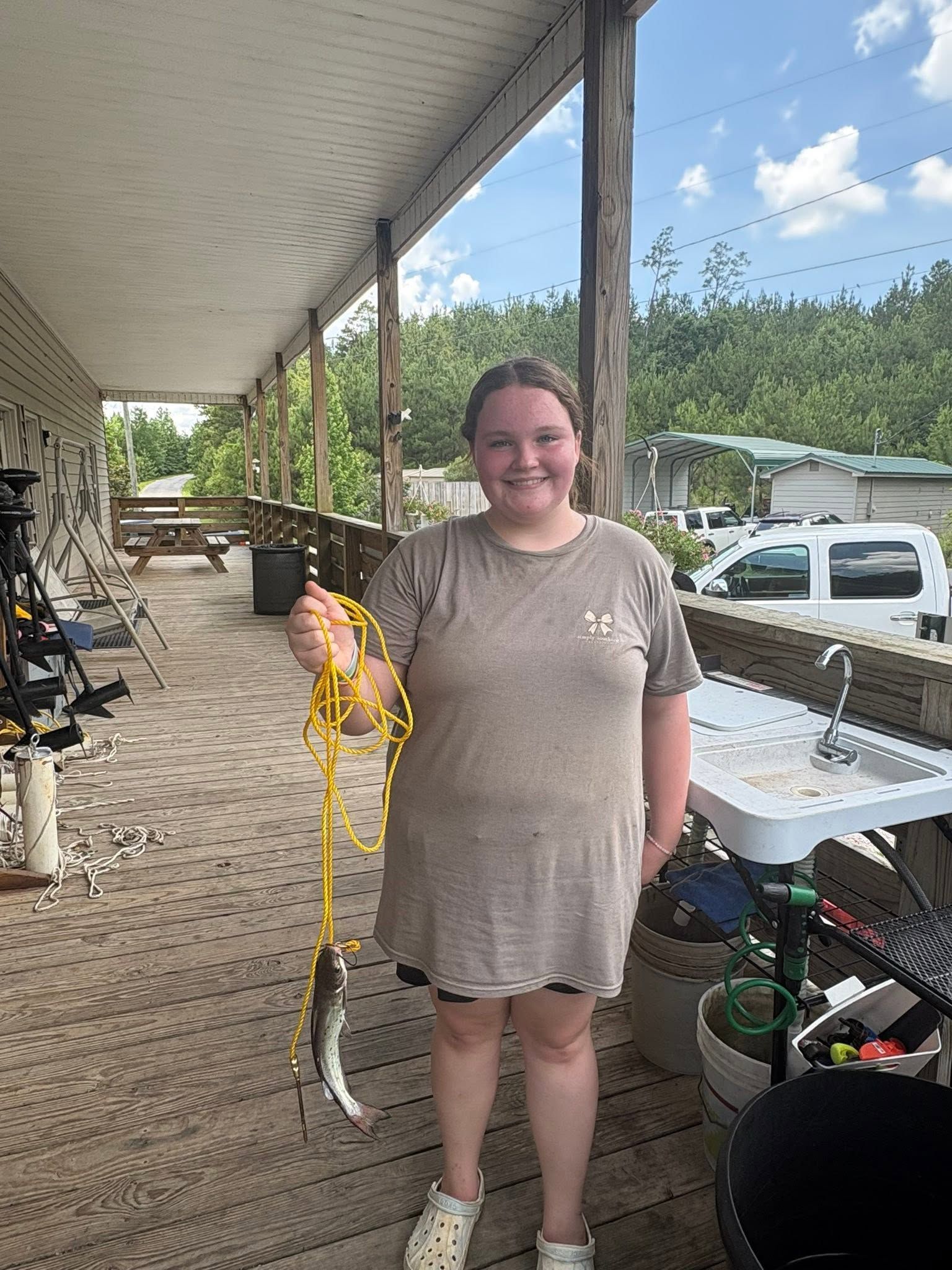 Person on a porch holding a long snake, with parked vehicles and trees in the background.