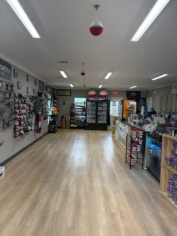 Bright retail store interior with wood flooring, fluorescent lights, and shelves of merchandise.