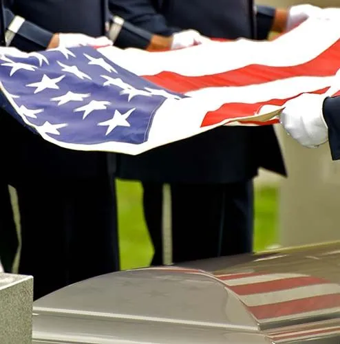 Uniformed honor guards in white gloves hold an American flag over a casket during a military funeral ceremony.