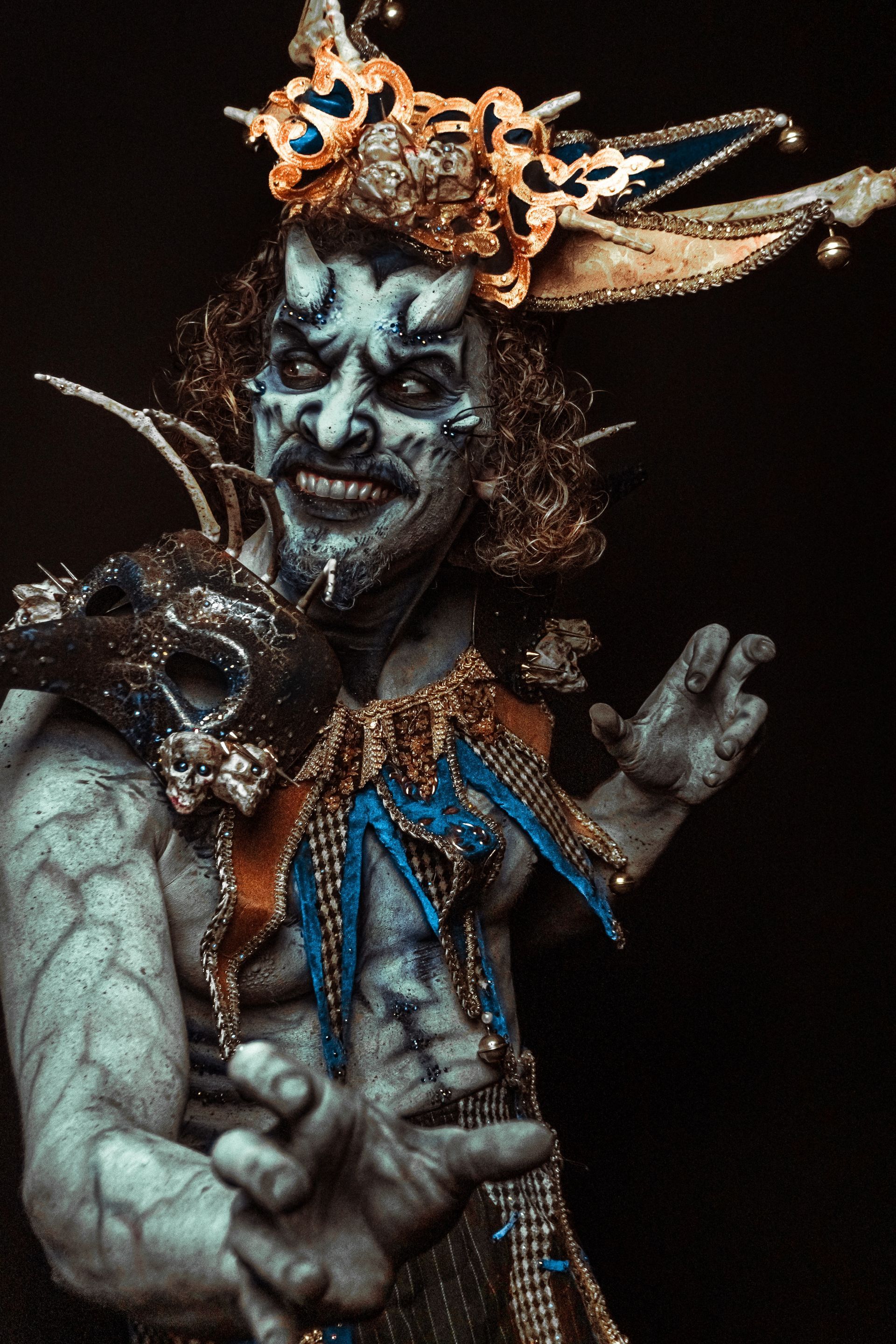 A man in a clown costume is holding a mask.