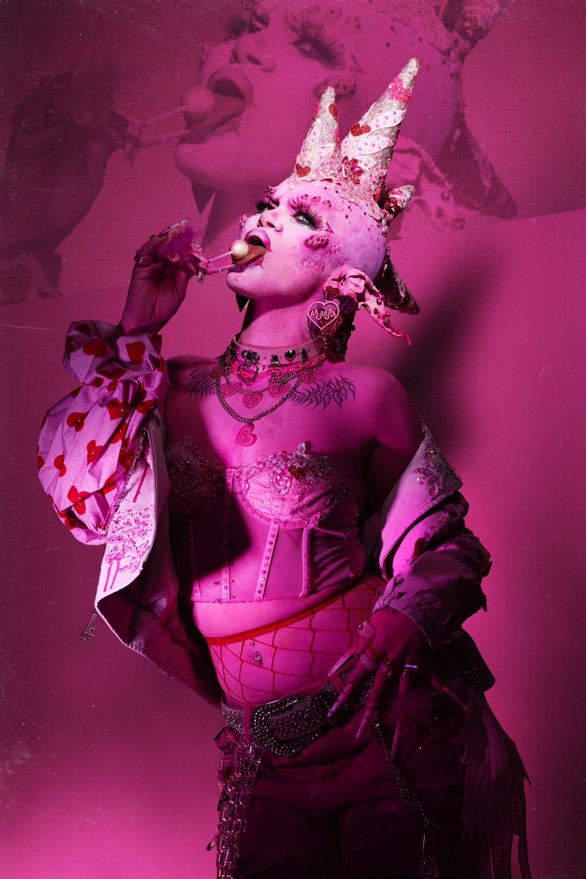 A woman with a crown on her head is standing in front of a pink wall.