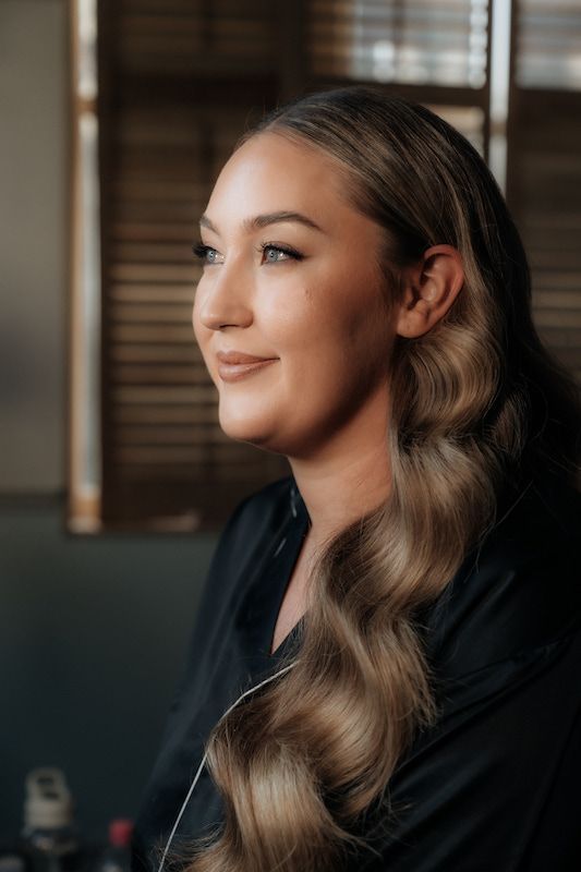 A woman with long hair is sitting in front of a window and smiling.