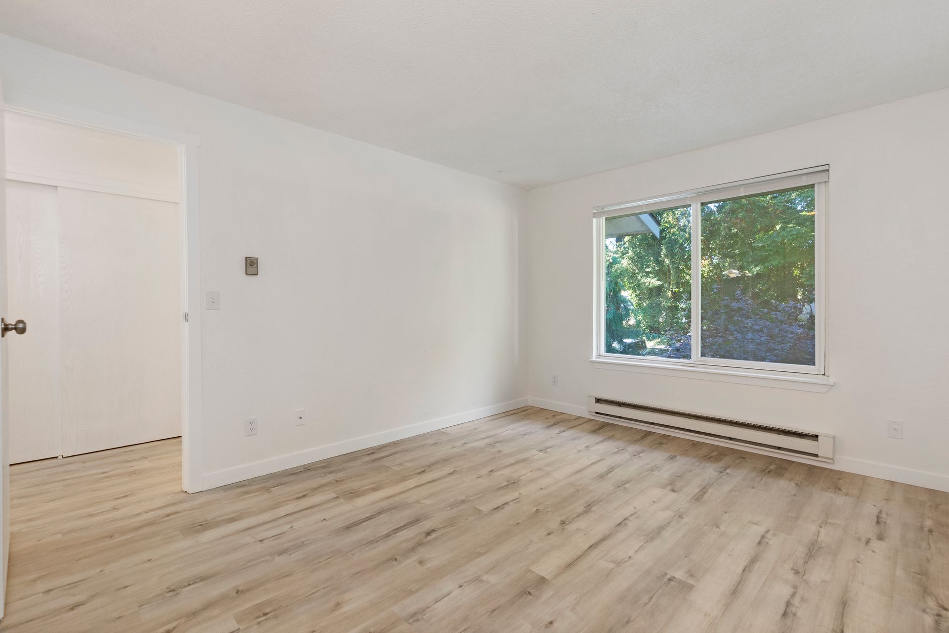 an empty living room with hardwood floors and a large window .