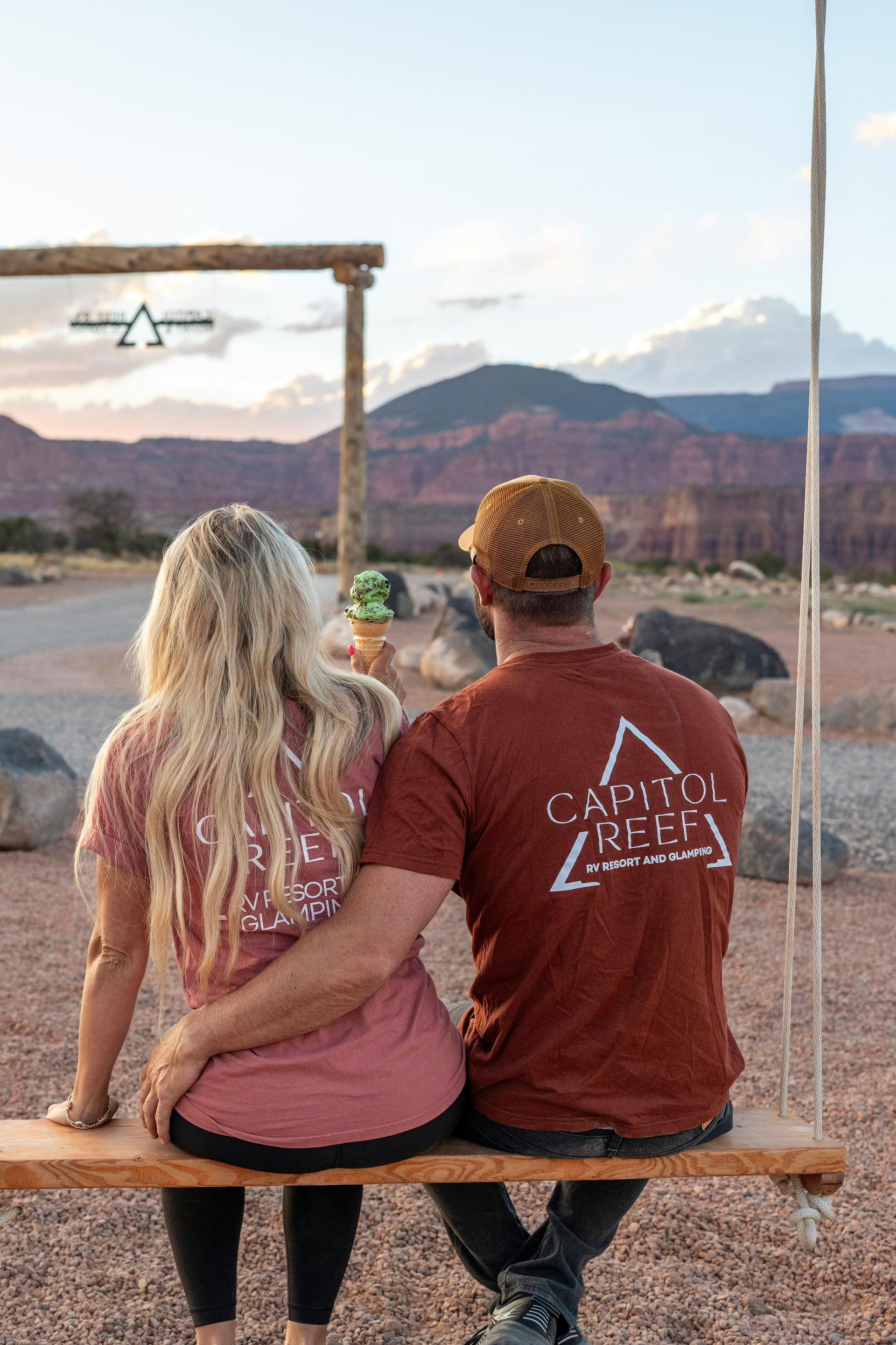 Couple sitting on swing, back to camera, wearing Capitol Reef shirts, with mountains in the background.