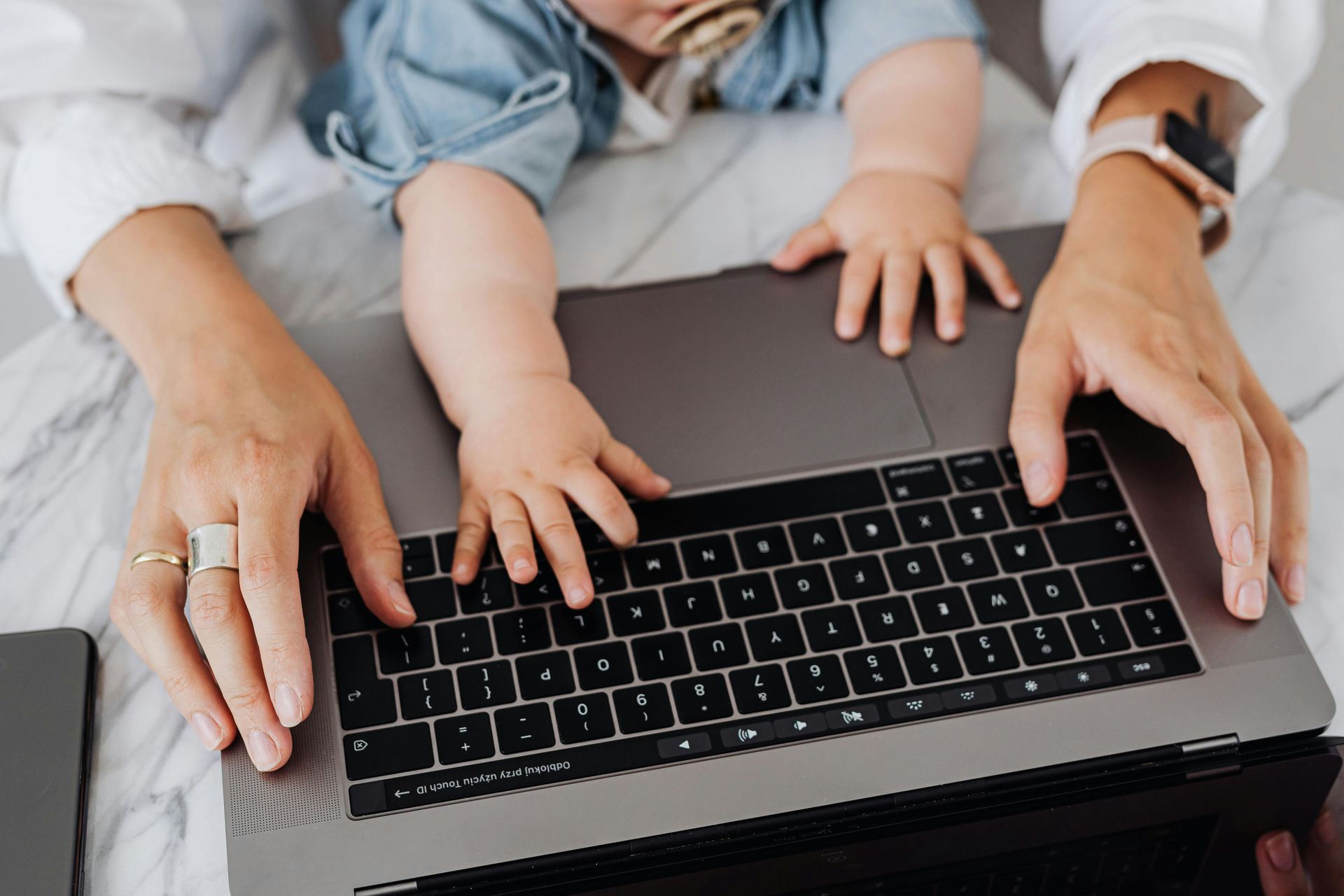 Woman and baby's hands on laptop keyboard, baby wearing a pacifier.