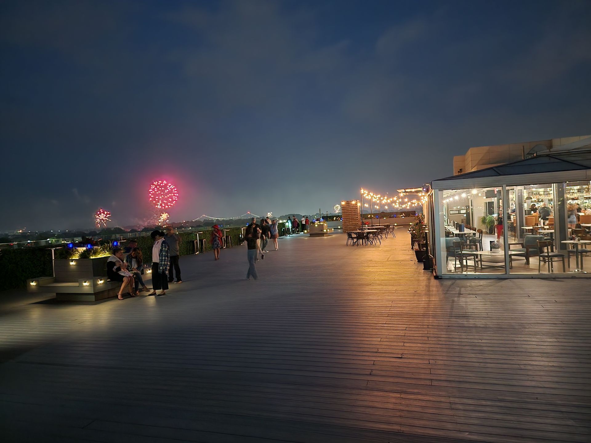 A group of people are standing on a pier at night watching fireworks.