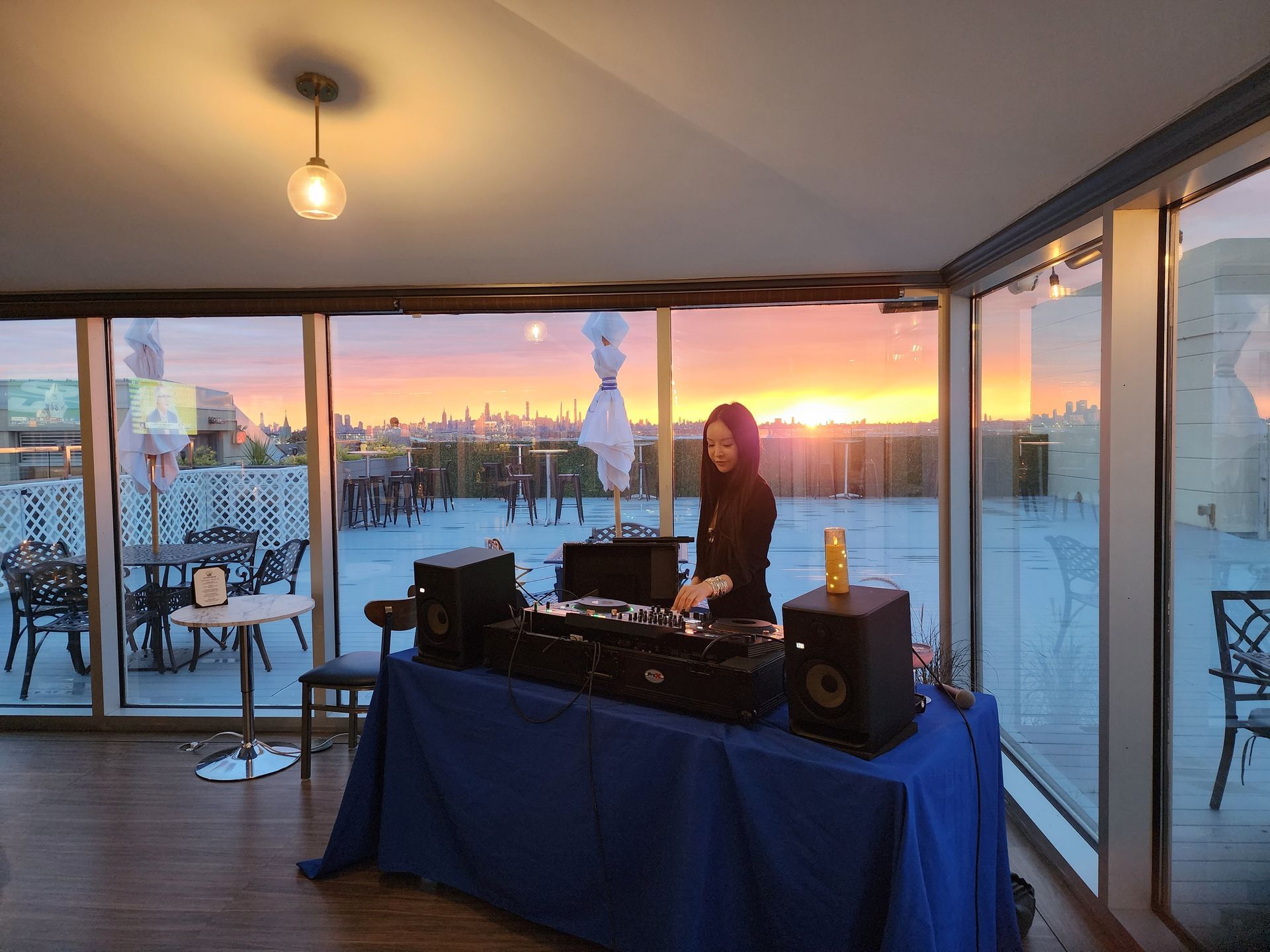 A woman is playing music on a dj set in a room with a sunset in the background.