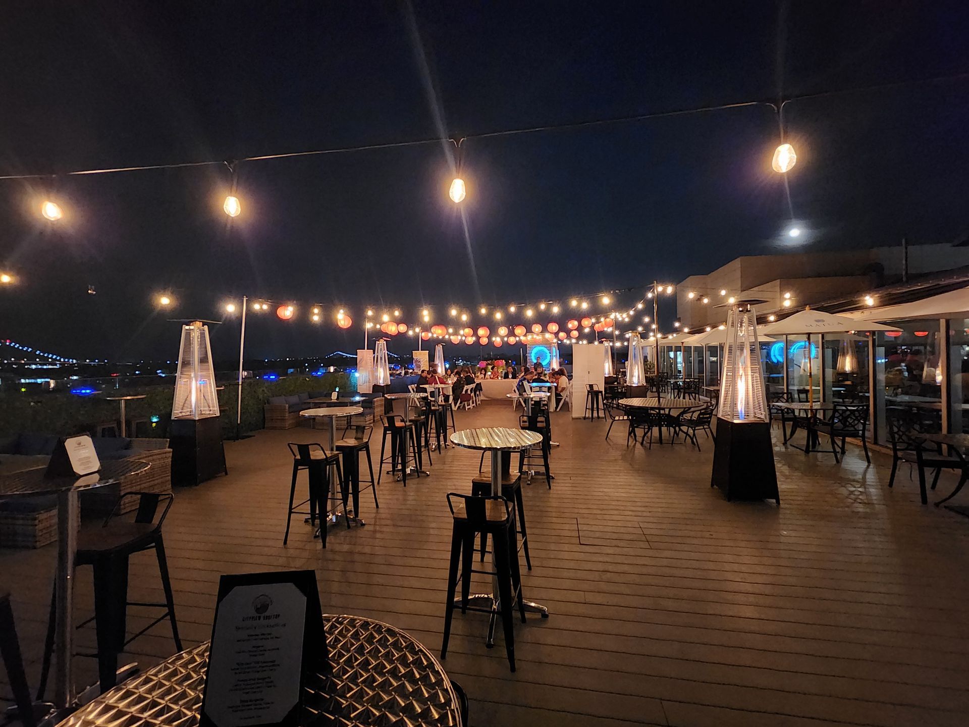 A patio with tables , chairs and heaters at night.