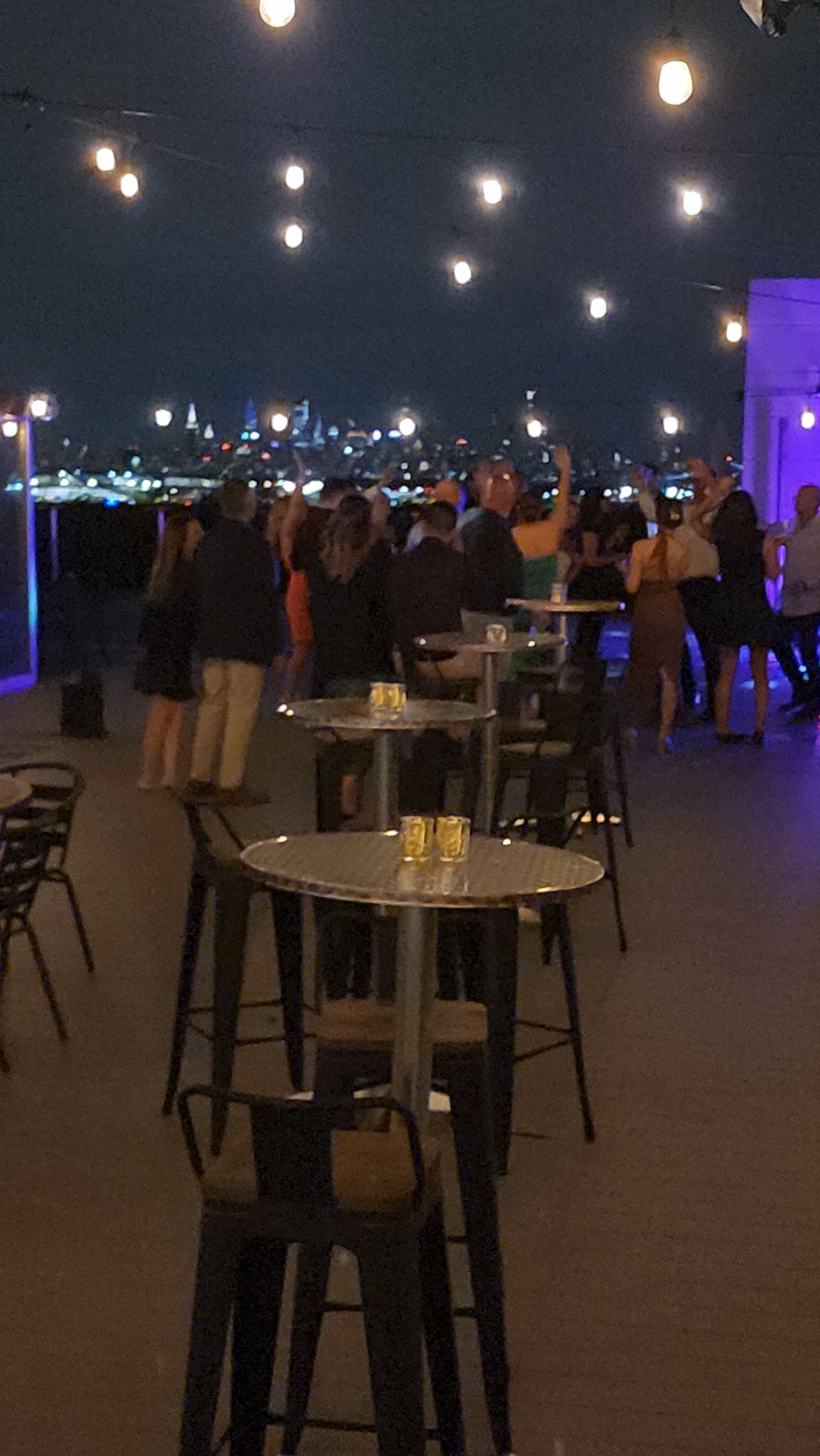 A group of people are standing around tables in a room at night.