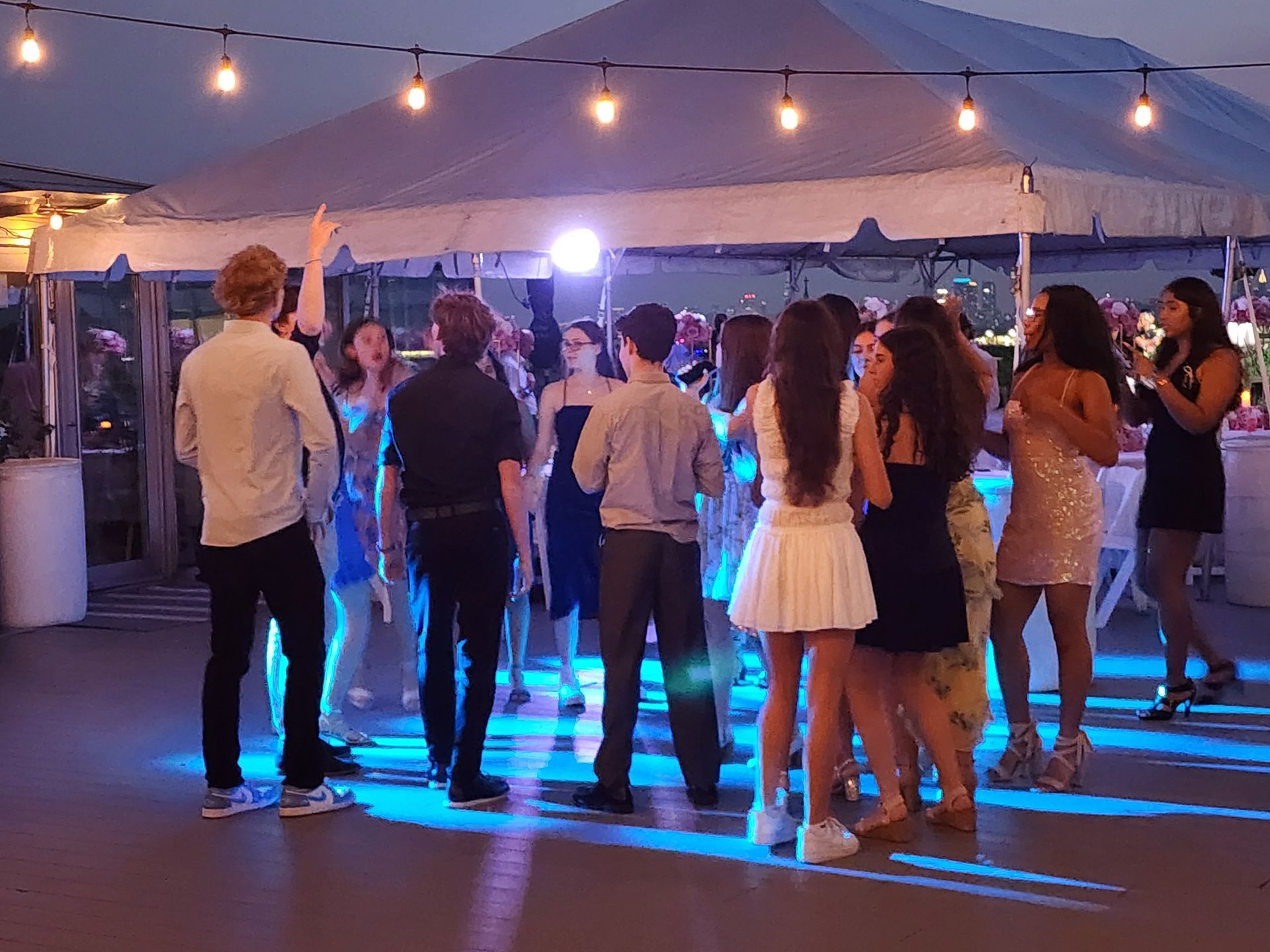 People dancing under a tent at night with string lights. Blue and white lighting.