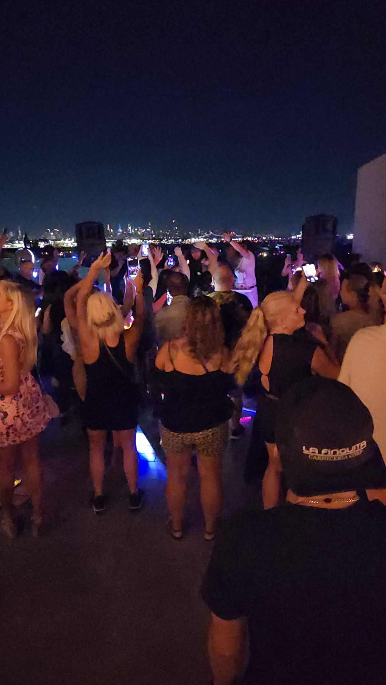 People dancing at a nighttime outdoor event; city lights visible in the distance.