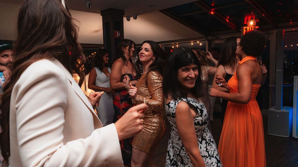 People dancing at a party; various cocktail dresses, smiles, and laughter. Evening setting with ambient lighting.