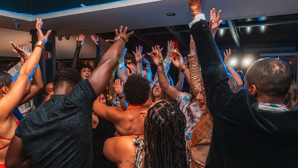 People dancing with arms raised in a brightly lit space. Party atmosphere, celebratory.