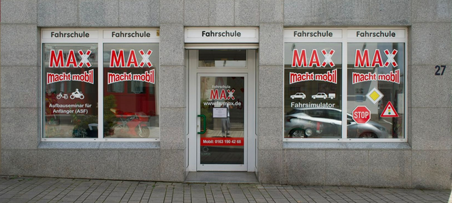 Fassade des Gebäudes mit der Fahrschule MAX Fahrschule, mit Schildern und Verkehrszeichen. Hausnummer 27 an der Seite.