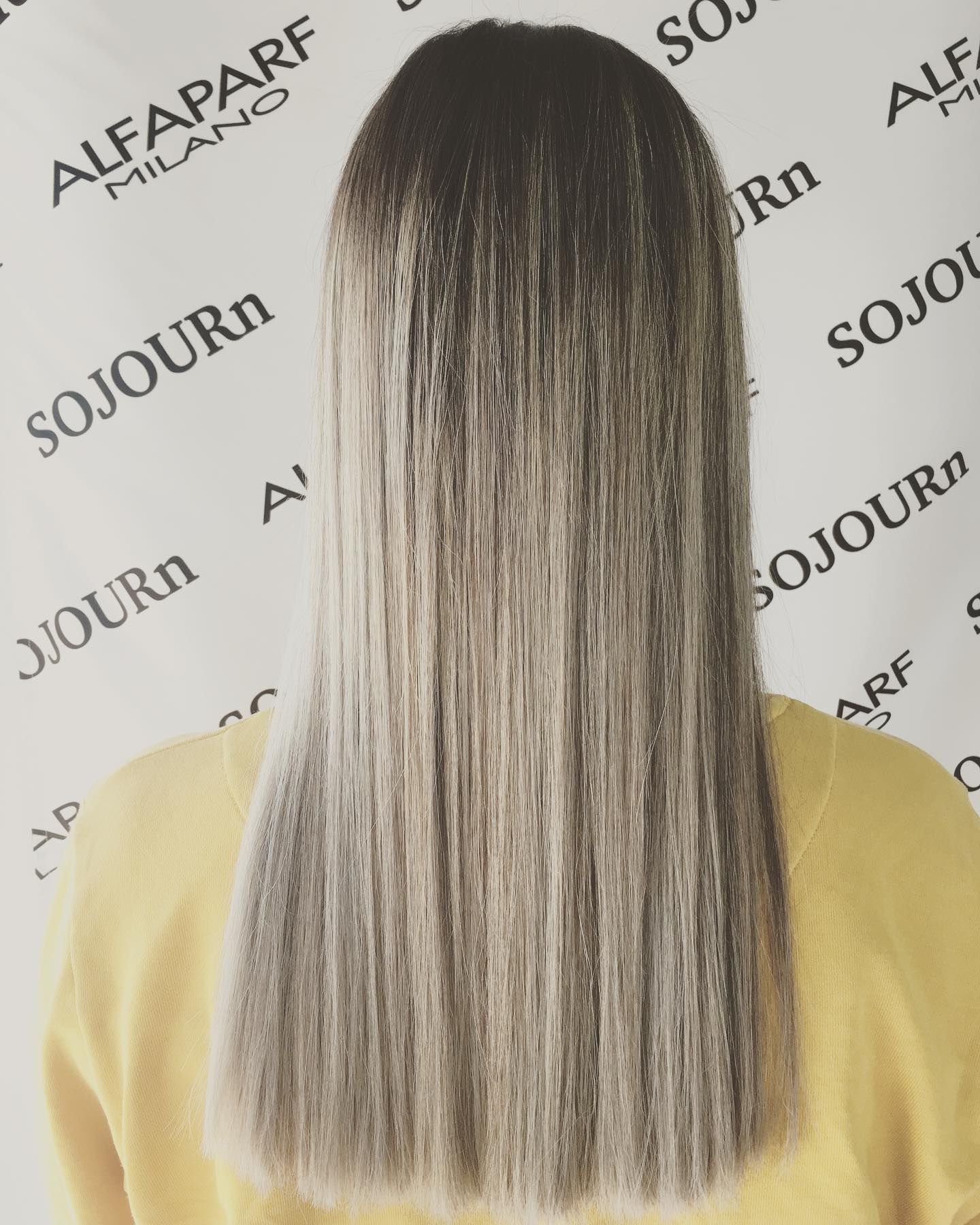 A woman with long hair is standing in front of a sign that says alfaparf milano