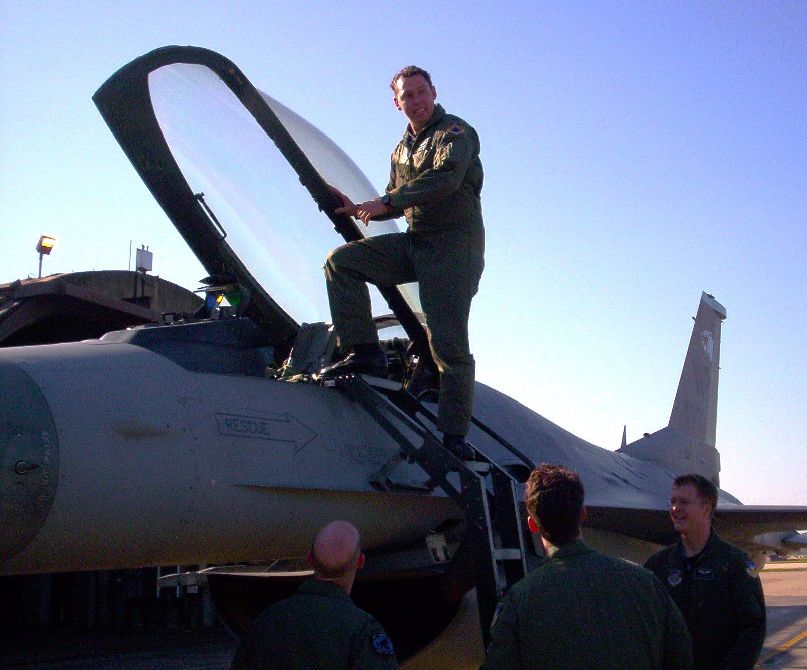 A man in a military uniform climbs into the cockpit of a fighter jet