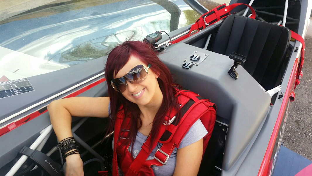 A woman wearing sunglasses and a red vest is sitting in a car.