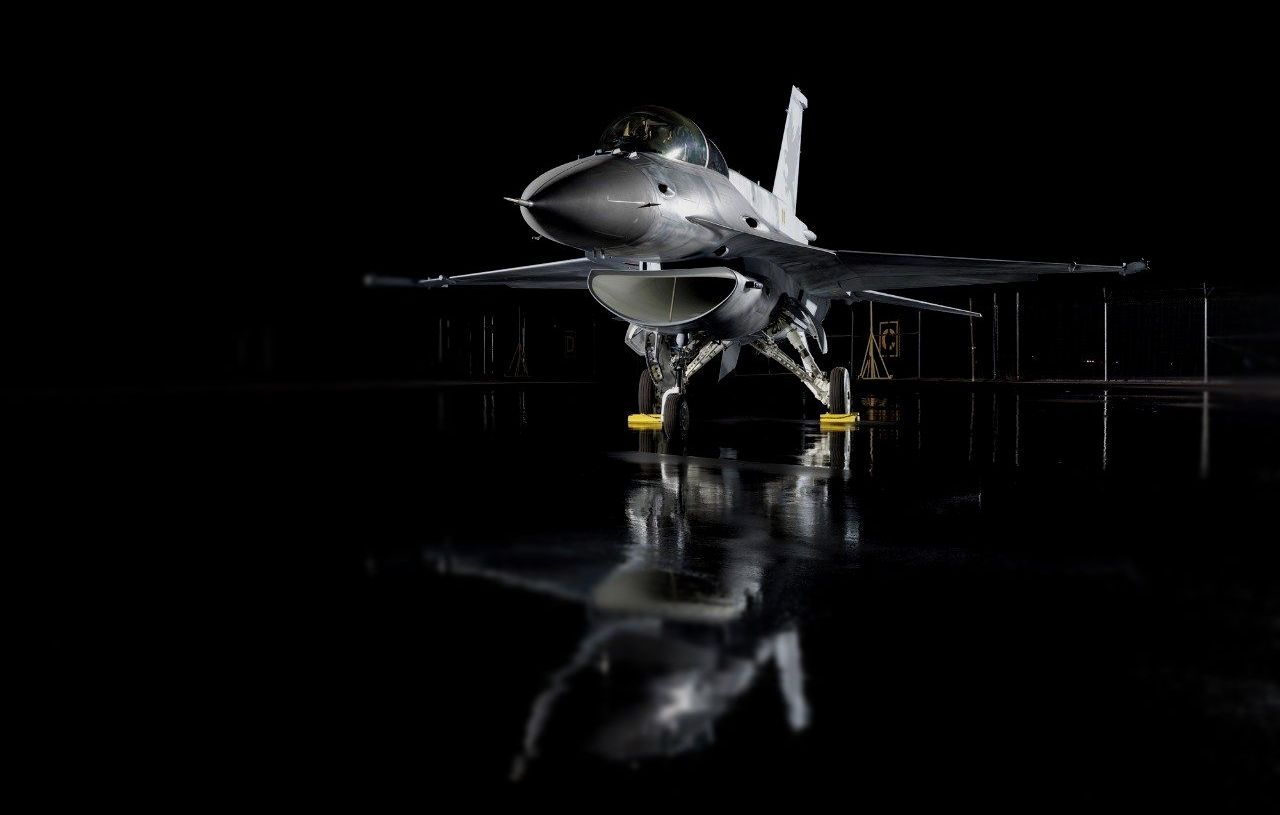 A fighter jet is parked in a hanger at night.