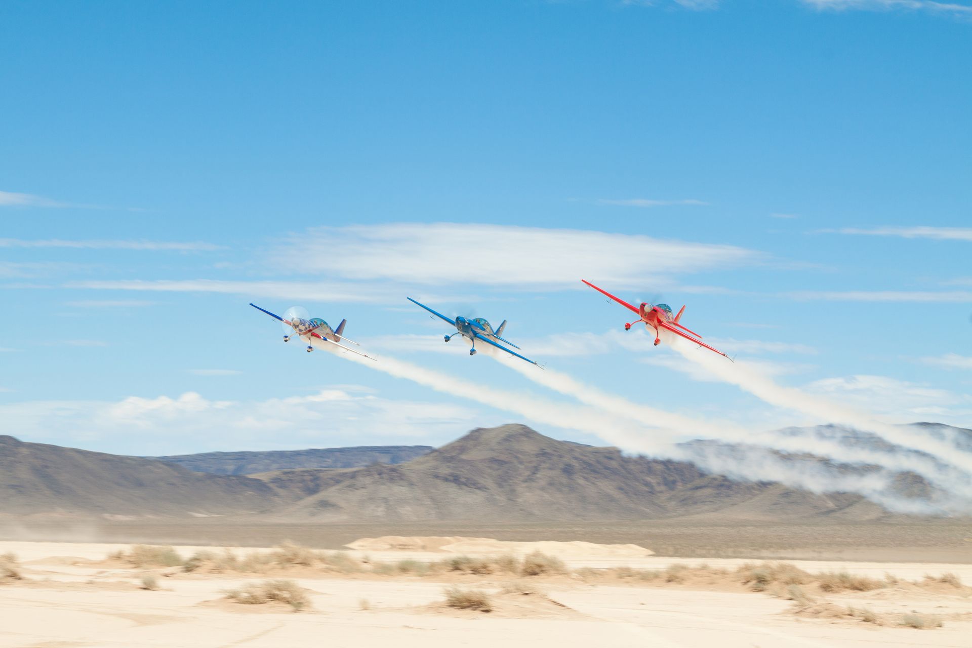 Three Sky Combat Ace stunt planes flying low over the Mojave desert with smoke on